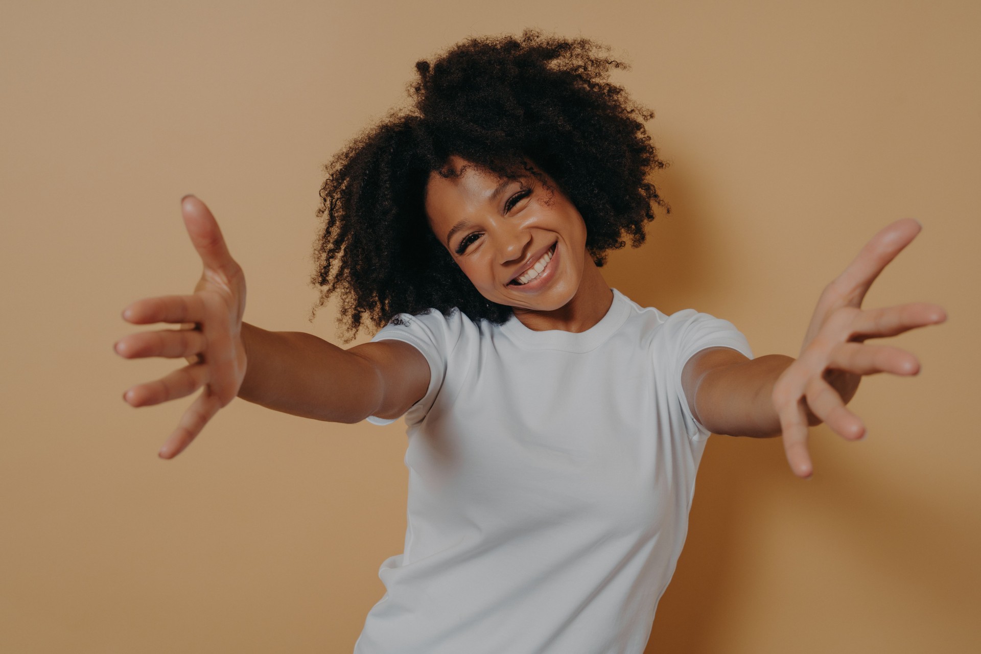 Happy friendly African American woman dressed in white shirt offering hugs, welcoming client